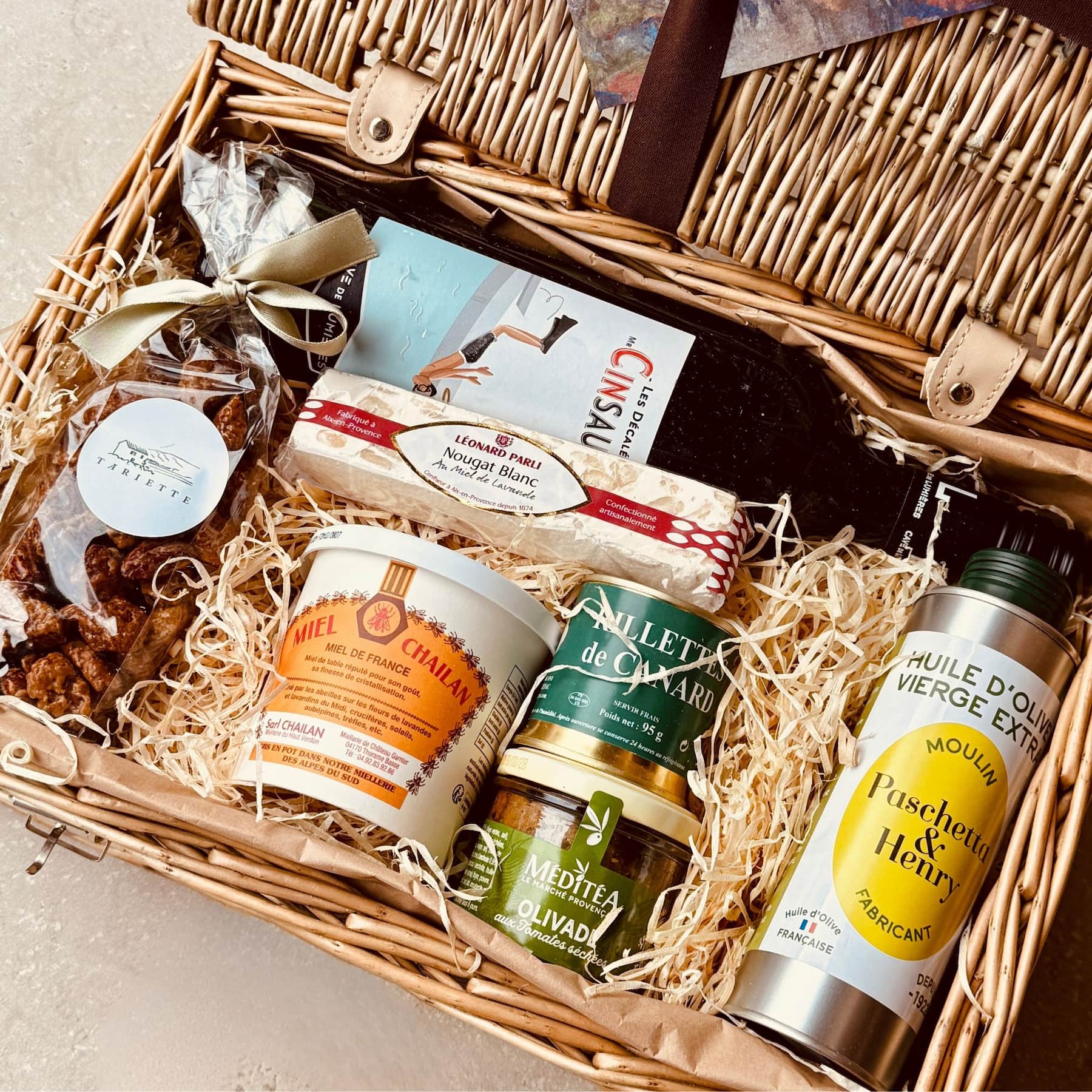 Gift basket with various items including a bottle of olive oil, a jar of spread, and a box of cookies.