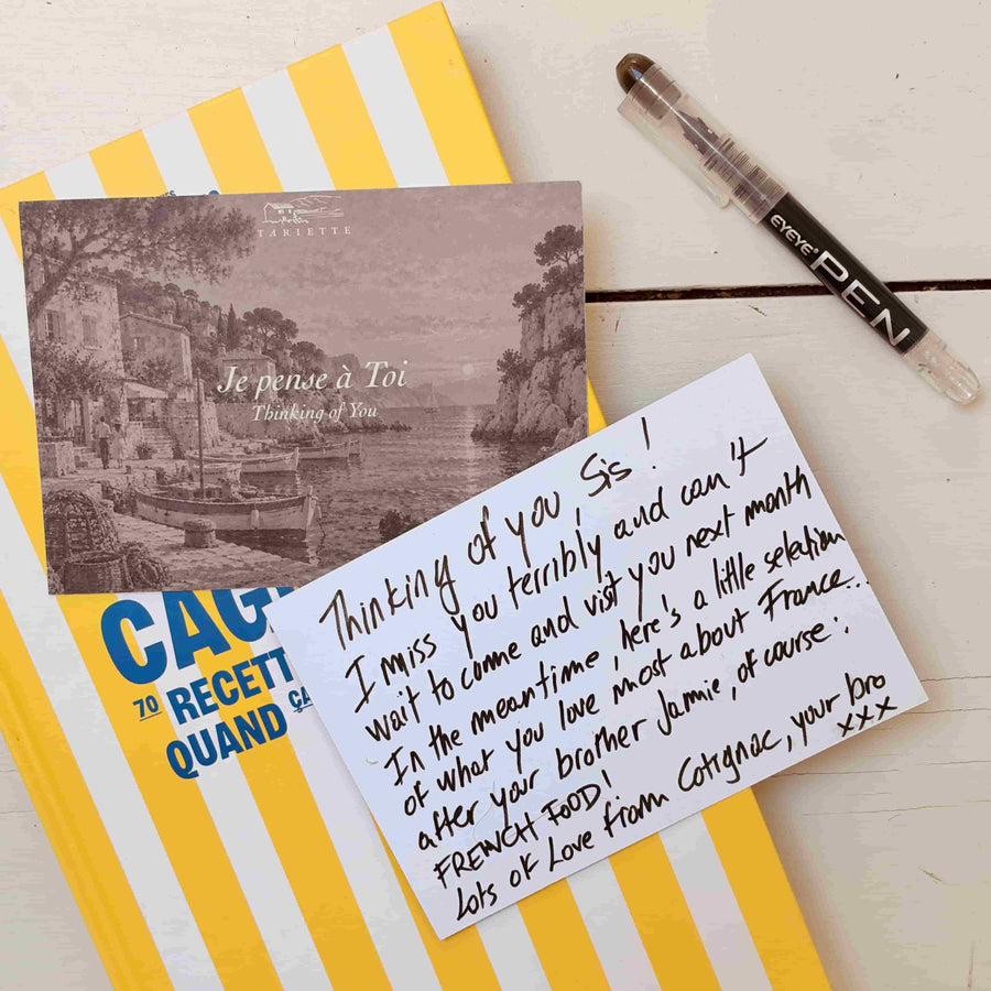 Tariette Thinking of You postcard beside a handwritten personal message, with a striped French cookbook and pen.