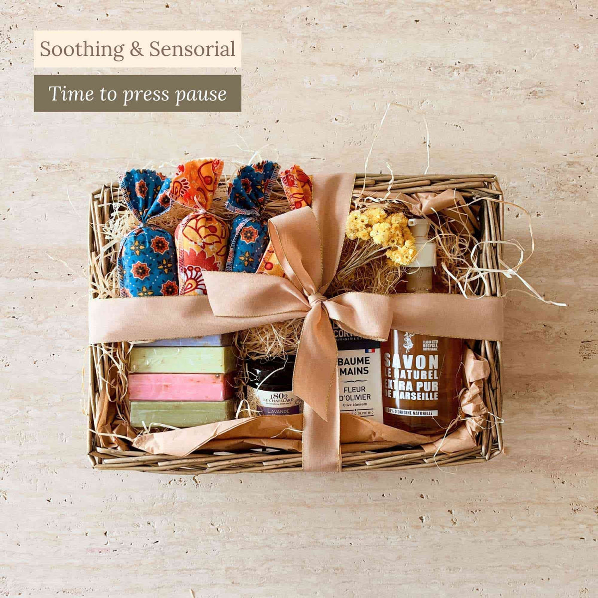 Tariette Les Bains self-care gift basket with Marseille soaps, hand balm, liquid soap, lavender bags, candle and flowers.