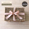 Tariette Manon sweet gift hamper in a closed wicker basket tied with a pale pink ribbon.