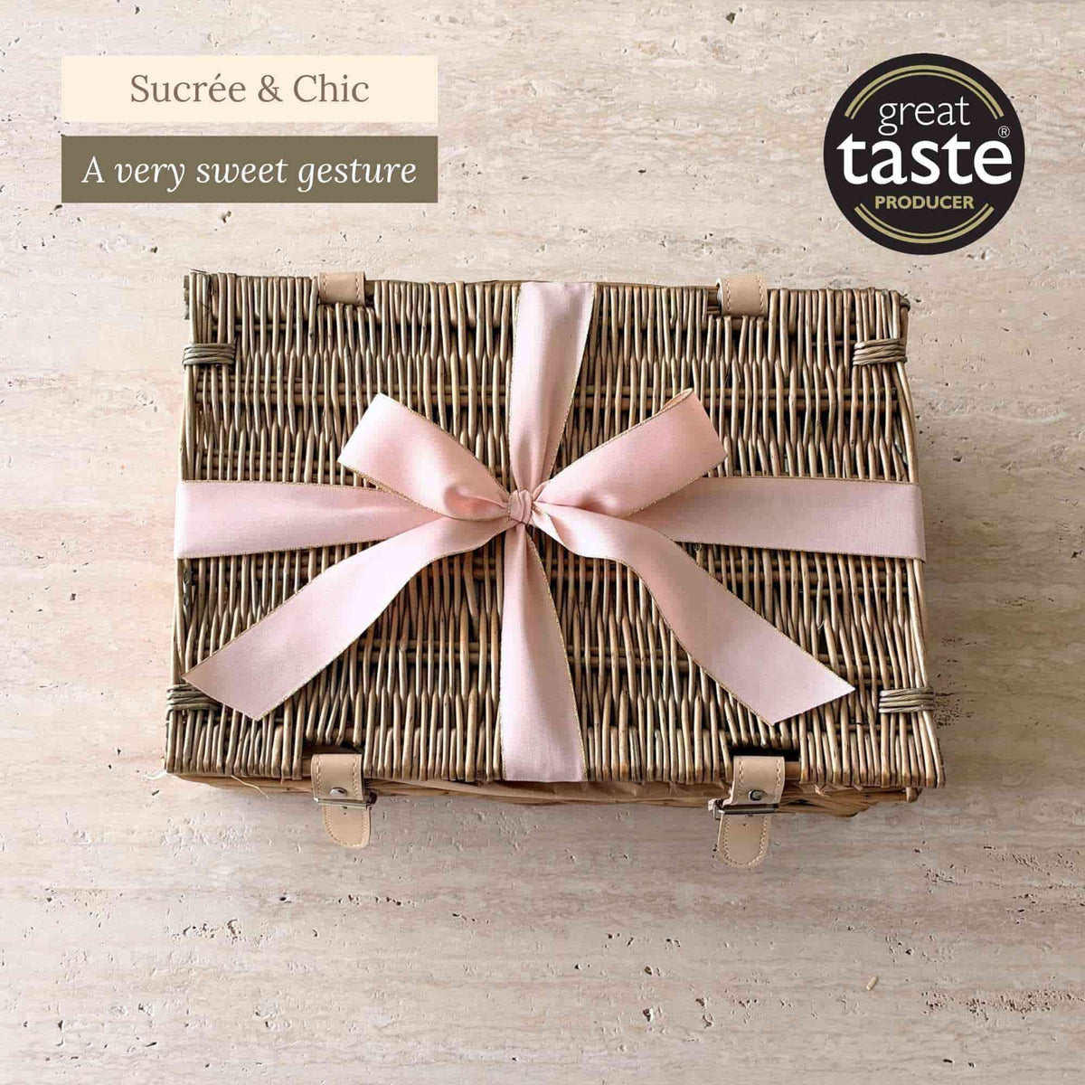 Tariette Manon sweet gift hamper in a closed wicker basket tied with a pale pink ribbon.