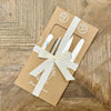Set of cutlery in a brown box with a white ribbon on a wooden surface