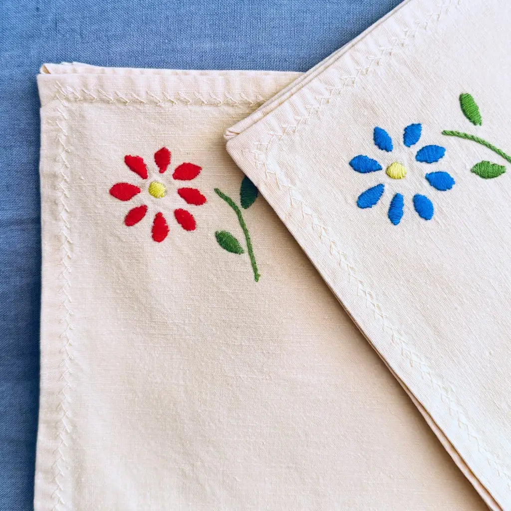 Each napkin is hand-embroidered in one corner, four with a bright blue flower and four with a vivid red, both with fresh green leaves.